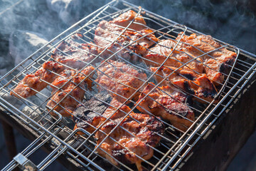 Browned pieces of meat in a metal grill on steaming coals during the preparation of barbecue in the country on May holidays. Healthy food cooked over an open fire.