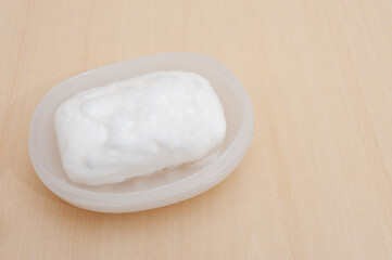 White soap with foam in soap dish. Isolated on beige background. Copy space. Horizontal shot.