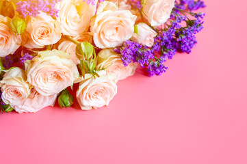a bouquet of cream roses and bright purple flowers in full bloom on a pink background with space for text. greeting card. flare