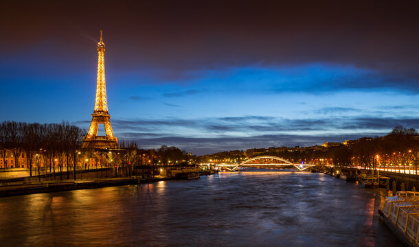 Paris, 75007, FRANCE - Mars 02, 2016: The Eiffel Tower illuminated at twilight with the Passerelle Debilly bridge and the Seine River banks (UNESCO World Heritage Site). Panoramic view
