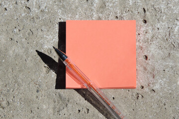   orange sticky note blank on concrete surface and pen, flat lay