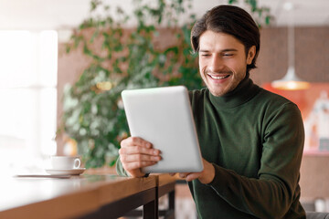 Cheerful man making video call via digital tablet, cafe interior