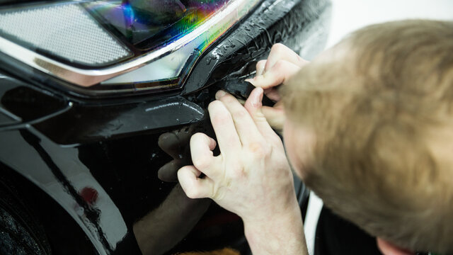Detailer applying a layer of paint protection film on a sports car
