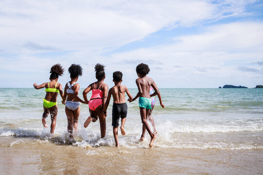 African American, Kids Group In Swimwear Enjoying Running To Play The Waves On Beach. Ethnically Diverse Concept. Having Fun After Unlocking Down From COVID 19. Summer Holidays On Beach With Friends