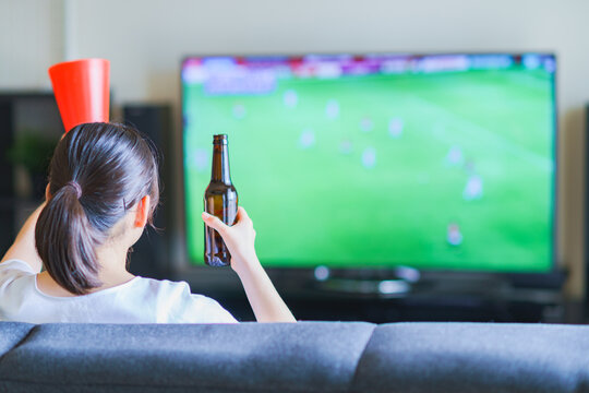 家でスポーツをテレビ観戦する若い女性のイメージ【プロサッカーの動画配信サービス】