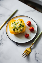Baked yellow pepper stuffed with couscous, green peas and feta cheese, cherry tomatos