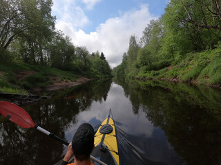 The men in a cap floats on a kayak on the forest quiet river, the beautiful landscape, a changeable weather, actively rows with an oar, beautiful reflection