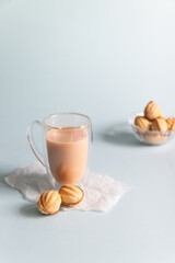 Hot coffee with milk in a glass cup and cookies on a blue background with copy space. Vertical photo