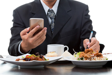 Businessman checking the news from mobile phone and taking memo while eating breakfast on white background