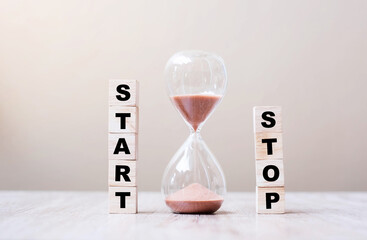Hourglass with START and STOP wooden cube blocks on table, Sand flowing through the bulb of...