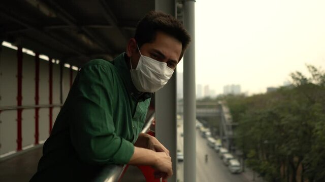 A man wearing mask protective for spreading of disease virus Covid-19 and air smog pollution with PM 2.5 standing on skywalk at chatuchak district in  Bangkok city, Thailand.