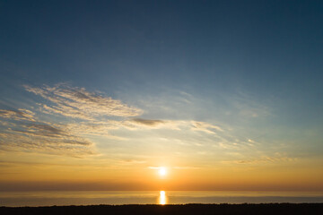 Sundown aerial view of evening sky with light clouds and sun descending to sea in Curonian spit near Nida, Lithuania