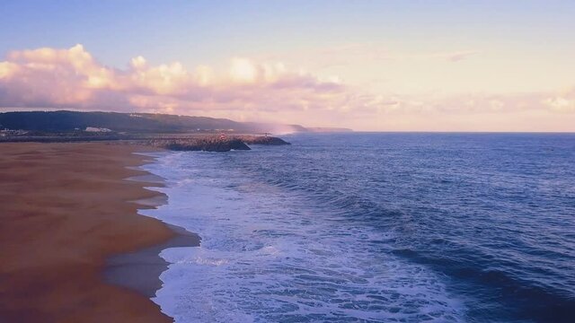 Flying over a sandy beach. Waves break on a sandy beach on the Atlantic coast, aerial View. Nazare, Portugal.