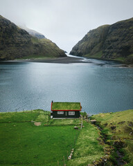 Lonely seaside house with green roof between the foggy green mountains, Faroe islands, Saksun village. Vertical nature photo.