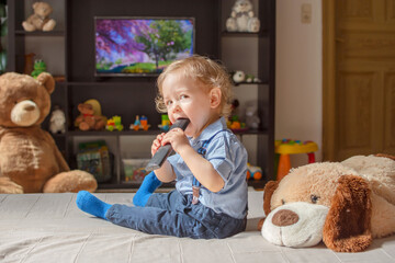 Cute baby boy and his dog plush toy watching TV sitting on a couch in the living room at home