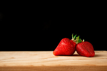 Two large red strawberries on a light wooden Board on a black background
