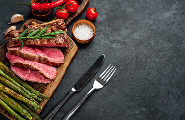 Fototapeta na wymiar Grilled beef steak with asparagus and spices on a cutting board on a stone background with copy space for your text