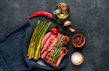 
Grilled beef steak with asparagus and spices on a black plate on a stone background