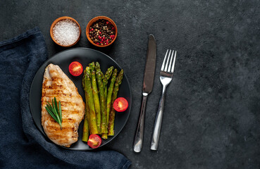 Grilled chicken breast with asparagus and spices on a black plate on a stone background with copy space for your text