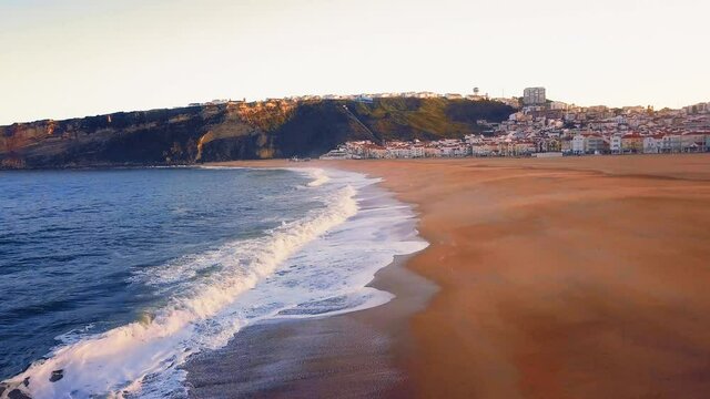 Flying over a sandy beach. Waves break on a sandy beach on the Atlantic coast, aerial View. Nazare, Portugal.