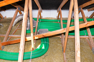 Ventilation for energy recovery in the home, visible collector and green flexible pipe connection, arranged on roof trusses with visible rock wool.
