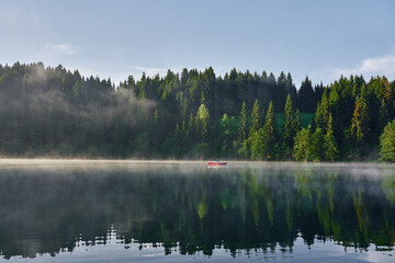 Man is rowing a boat on the foggy lake Karagol / Karagöl at sunrise. Landscape photo was taken in Savsat / Şavşat, Artvin, Karadeniz / Black Sea region of Turkey