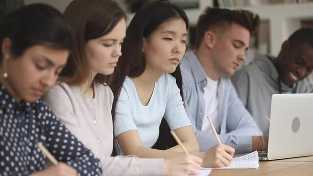 Focused serious asian girl student with multi ethnic international people group study in college sit in row at desk write notes listen to lecturer during university class lecture lesson in classroom