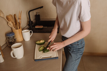 cropped view of woman holding knife while cutting tasty avocado near cups