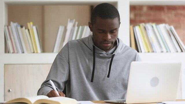 Focused african black male student using laptop search information internet course study online e learning in app typing on computer make notes write essay prepare for test exam sit at library desk