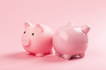 Two pink piggy banks on a pink background.