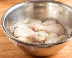Chicken drumstick soaked in mayonnaise. A bowl of chicken in the sauce is covered with a transparent kitchen bag
