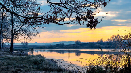 Sunrise over the river, frost-covered grass   on the shore river in the morning, reflection of the sky in the river