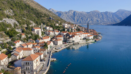 Fototapeta na wymiar Perast Montenegro: Old medieval town featuring stone houses with red roofs, by beautiful Kotor bay, on the coast of Adriatic sea. Crystal clear rippled water surface. Sunny day. Aerial footage.