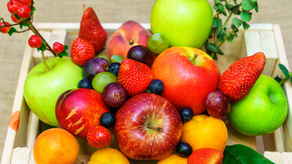 Set of berries and fruits in wooden box. Apple, strawberry, grape, berry and peach on a red brick background.