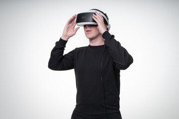 Young man in black shirt uses VR glasses in white studio, dreamily looking away and touches glasses with hands, waist-height portrait