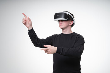 Young man in black shirt uses VR glasses in white studio, dreamily looking away and pointing his fingers up, waist-height portrait