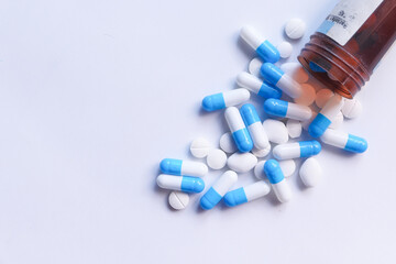 Close up of colorful capsules spilling from container on white background 