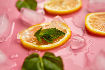 Composition with cut citrus fruits on pink background. Creative summer background composition with lemon slices, leaves mint and ice cubes. Minimal top down lemonade drink concept.Top view