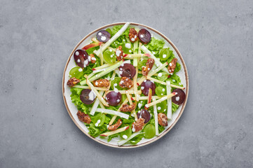Waldorf Salad on white plate on gray concrete background. Waldorf salad is american cuisine dish with lettuce, grapes, apple, celery. Vegetarian healthy meal.