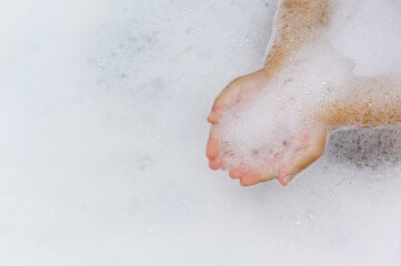 the child plays in a bathtub filled with white foam, palms hold foam for bathing