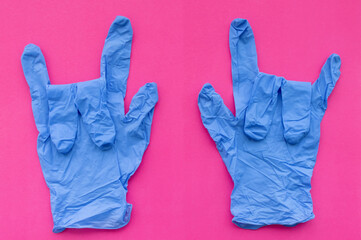Medical gloves in blue on a pink background show the "Sign of the horns"gesture. Selective focus.