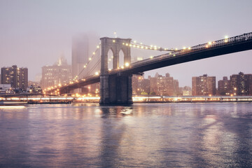 Fototapeta na wymiar Brooklyn Bridge on a foggy night, color toned picture, New York City, USA.