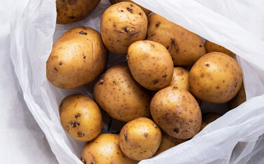 A pile of unwashed potatoes lies in a white bag