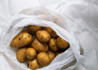 A pile of unwashed potatoes lies in a white bag