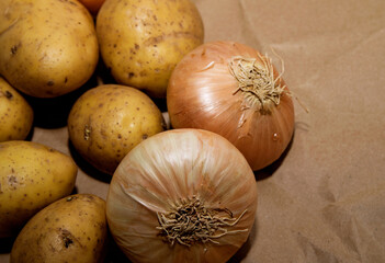 Unwashed potatoes and onions lie on a paper bag