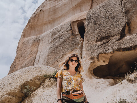 young woman with sunglasses in front of a cave in the Turkish Capadoccia
