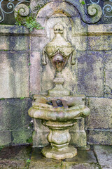 Fountain of São Miguel (Portuguese: Chafariz de São Miguel) in Porto Portugal. Made of stone blocks, with multiple ornaments. Black mold and green moss growing on wet surfaces.