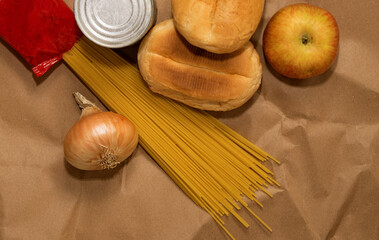 apple, spaghetti, onions, bread and canned goods lie on a paper bag