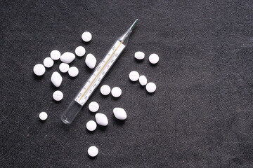 Fototapeta na wymiar medical thermometer and white pills on black background 