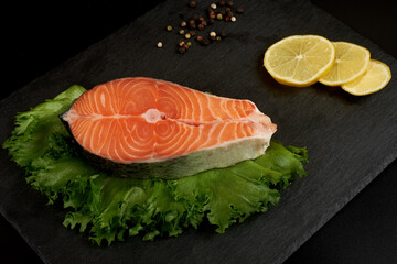 Salmon steak raw fish with a lemon prepared for cooking. Top view on black slate table.